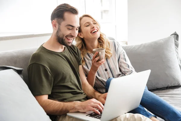 Feliz emocionado joven pareja amorosa sentada en el sofá en casa utilizando el ordenador portátil . —  Fotos de Stock