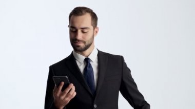 Siyah takım elbise ve mavi kravat mutlu genç işadamı gri arka plan izole üzerinde akıllı telefon kullanırken gülümseyen