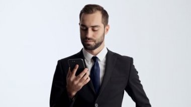 Siyah takım elbise ve mavi kravat konsantre genç işadamı kazanan jest yapma ve gri arka plan izole üzerinde akıllı telefon kullanırken çığlık