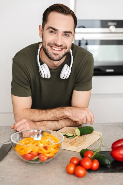 Счастливый молодой красивый мужчина позирует на кухне дома, готовит музыку в наушниках . — стоковое фото