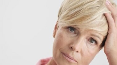 Gri arka plan izole üzerinde kameraya bakarken konsantre ciddi sarışın yaşlı kadın saçlarını sabitleme Kırpılmış görünümü