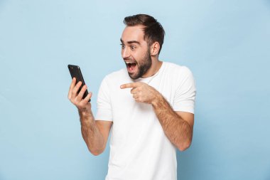Mavi duvar arka plan üzerinde izole cep telefonu kullanarak yakışıklı heyecanlı genç adam.