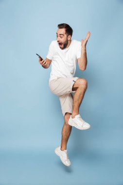 Mavi duvar arka plan üzerinde izole cep telefonu kullanarak yakışıklı heyecanlı genç adam.