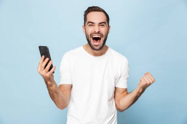 Mavi duvar arka plan üzerinde izole cep telefonu kullanarak yakışıklı heyecanlı genç adam.