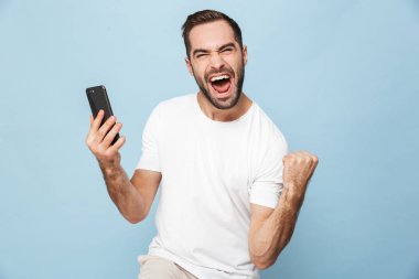 Mavi duvar arka plan üzerinde izole cep telefonu kullanarak yakışıklı heyecanlı genç adam.