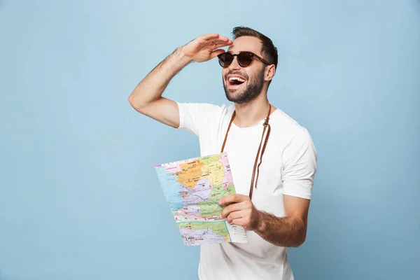 Guapo joven turista posando con mapa aislado sobre fondo de pared azul . — Foto de Stock