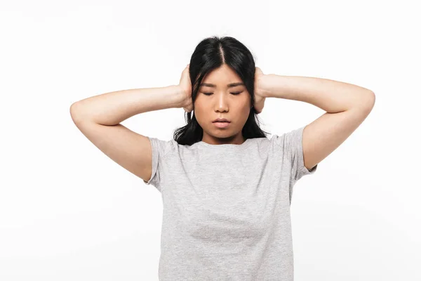 Ασίας λυπημένη όμορφη νεαρή γυναίκα που θέτουν απομονωμένα πάνω από λευκό τοίχο φόντο καλύπτοντας τα αυτιά. — Φωτογραφία Αρχείου