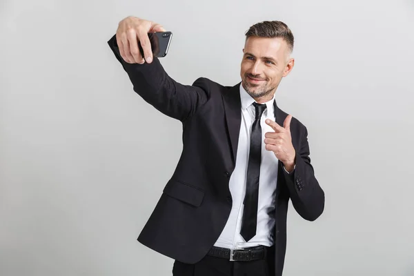 Imagem de empresário caucasiano bem sucedido em terno formal apontando dedo e tomando selfie no celular — Fotografia de Stock