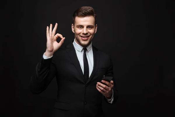 Retrato de jovem empresário bonito vestido em terno formal usando celular e gesto ok sing — Fotografia de Stock