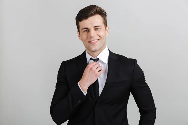 Image of confident young businessman in formal suit touching his tie and smiling at camera — Stock Photo, Image