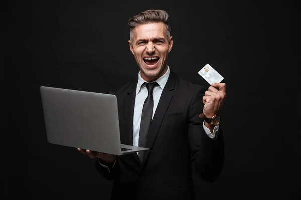 Retrato de hombre de negocios caucásico gritando vestido con traje formal sosteniendo computadora portátil y tarjeta de crédito — Foto de Stock