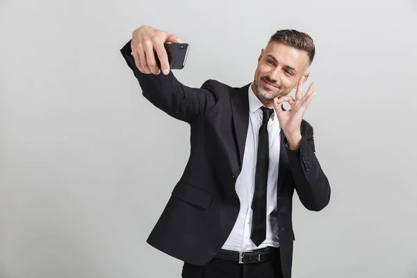 Immagine di successo uomo d'affari sorridente in abito formale gesturing ok cantare mentre prende selfie sul cellulare — Foto Stock