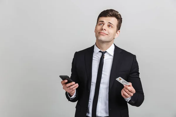 Wizerunek przemyślany brunetka biznesmen w formalne garnitur Dreaming trzymając telefon komórkowy i karty kredytowej — Zdjęcie stockowe