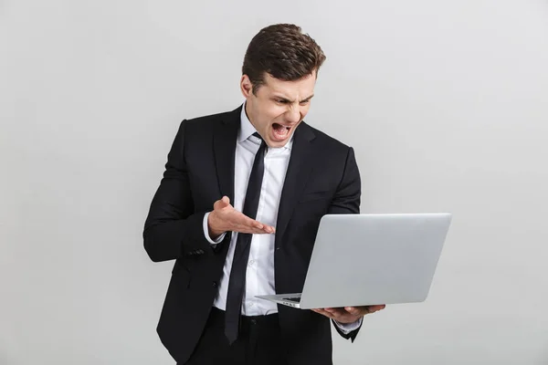 Retrato de estresado joven empresario irritado en traje de oficina gritando mientras sostiene el ordenador portátil —  Fotos de Stock