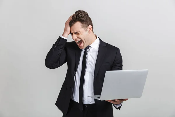 Retrato de descontento indignado joven empresario en traje de oficina gritando mientras sostiene el ordenador portátil — Foto de Stock