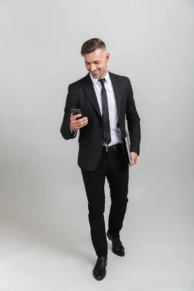 Photo de heureux homme d'affaires adulte en costume formel souriant tout en tenant ordinateur portable et téléphone portable — Photo