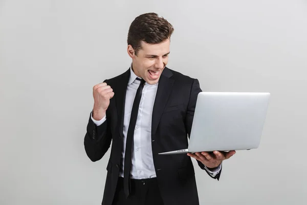 Imagen de un alegre empresario emocionado en traje formal celebrando el triunfo mientras sostiene el portátil —  Fotos de Stock