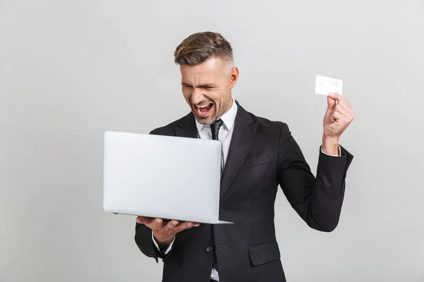 Imagen de hombre de negocios adulto alegre en traje formal sorprendente mientras sostiene el ordenador portátil y la tarjeta de crédito — Foto de Stock