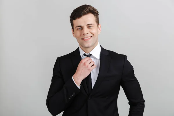 Image d'un jeune homme d'affaires confiant en costume formel touchant sa cravate et souriant à la caméra — Photo