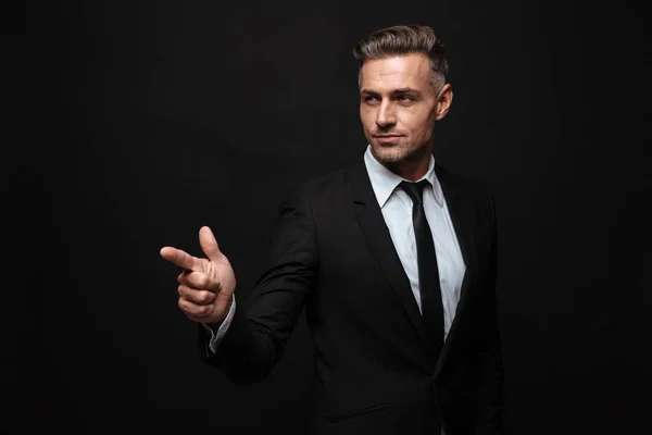 Retrato de homem de negócios inteligente sério vestido em terno formal apontando o dedo e olhando para o lado — Fotografia de Stock