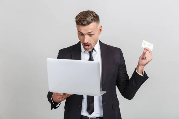 Εικόνα του ενθουσιασμένο ενήλικα επιχειρηματία σε επίσημο κοστούμι έκπληξη, ενώ κρατώντας φορητό υπολογιστή και πιστωτική κάρτα — Φωτογραφία Αρχείου