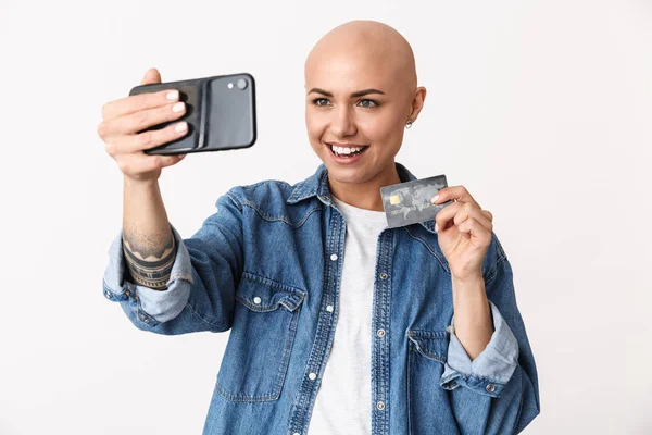 Gelukkige kale vrouw poseren geïsoleerd over witte muur achtergrond praten door mobiele telefoon neem een selfie Holding creditcard. — Stockfoto