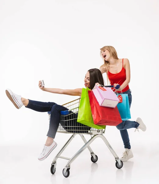 Полная длина двух веселых молоденьких девушек, делающих покупки вместе — стоковое фото