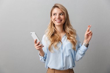 Mutlu genç güzel sarışın iş kadını cep telefonu kullanarak izole gri duvar arka plan poz.