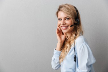 Mutlu genç güzel sarışın iş kadını mikrofon ile kulaklık giyen izole gri duvar arka plan poz.