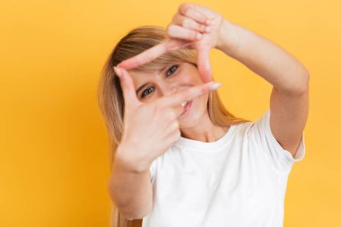 Mutlu genç güzel sarışın kadın beyaz rahat t-shirt fotoğraf çerçeve jest gösteren giymiş sarı duvar arka plan üzerinde izole poz.