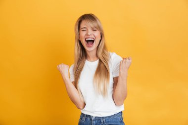 Neşeli genç heyecanlı şok sarışın kadın sarı duvar arka plan üzerinde izole poz kazanan jest yapmak.