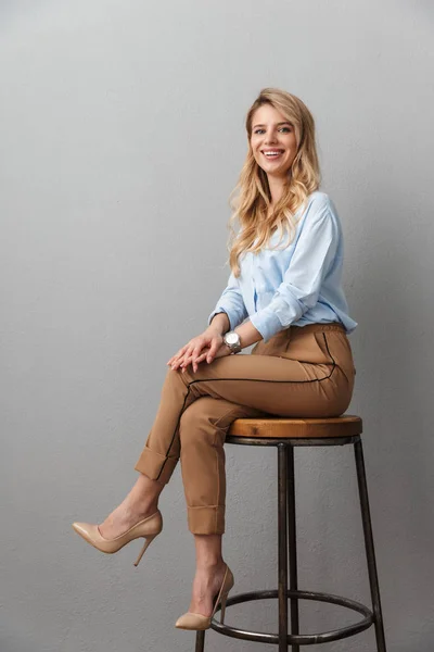 Femme d'affaires blonde posant isolé fond de mur gris assis sur tabouret . — Photo