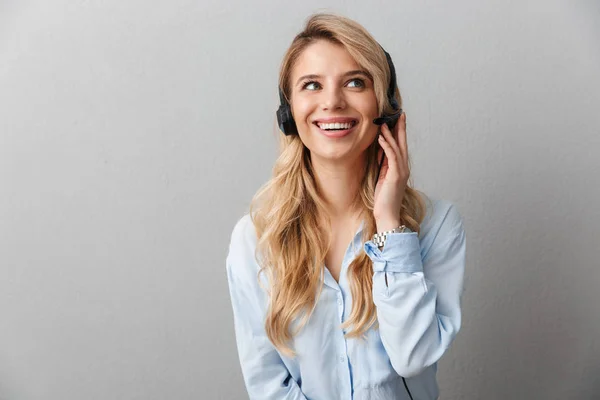 Feliz jovem mulher de negócios bonita loira posando isolado fundo de parede cinza usando fones de ouvido com microfone . — Fotografia de Stock