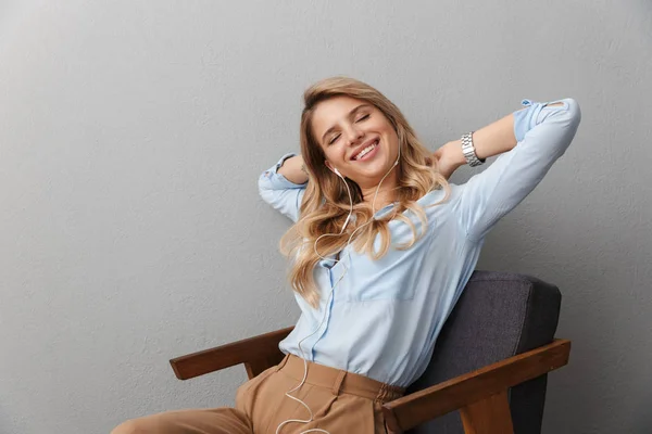 Lycklig ung Söt blond affärskvinna poserar isolerad grå vägg bakgrund lyssnar musik med hörlurar. — Stockfoto