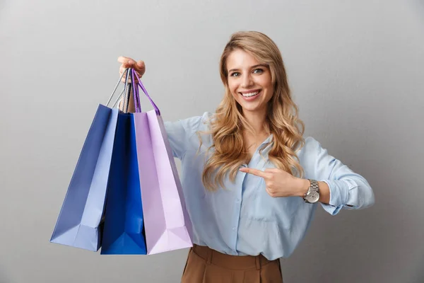Gelukkig opgewonden jonge mooie blonde zakenvrouw poseren geïsoleerde grijze muur achtergrond Holding shopping bags. — Stockfoto