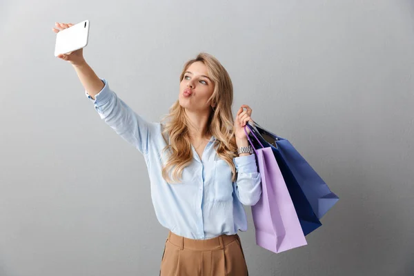 Gelukkig opgewonden jonge mooie blonde zakenvrouw poseren geïsoleerde grijze muur achtergrond Holding shopping bags. — Stockfoto