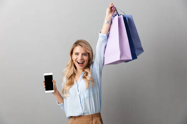 Glücklich aufgeregt junge hübsche blonde Geschäftsfrau posiert isoliert graue Wand Hintergrund mit Einkaufstaschen. — Stockfoto