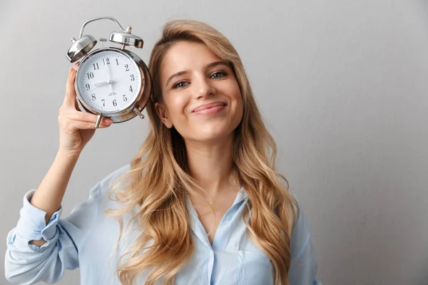 Unga vackra blonda affärskvinna poserar isolerad grå vägg bakgrund håller väckarklocka. — Stockfoto