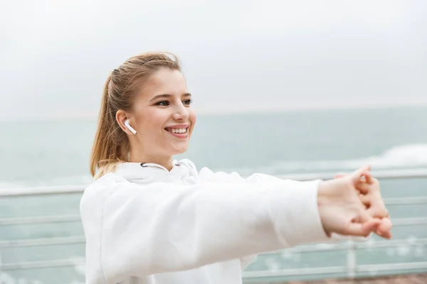 Bild av unga Fitness kvinna leende och stretching armarna medan du tränar nära havet — Stockfoto