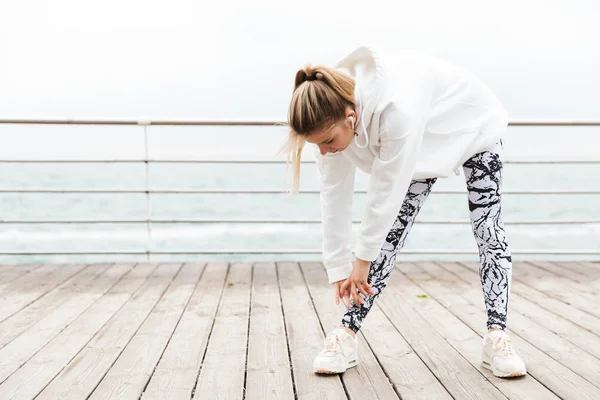 Deniz kenarında egzersiz yaparken atletik genç kadın bükme ve vücudunu germe Görüntü — Stok fotoğraf