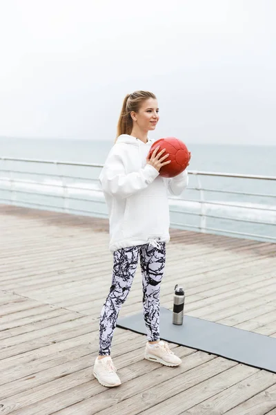 Bild av attraktiva atletisk kvinna gör övningar med Fitness boll medan du tränar nära havet — Stockfoto