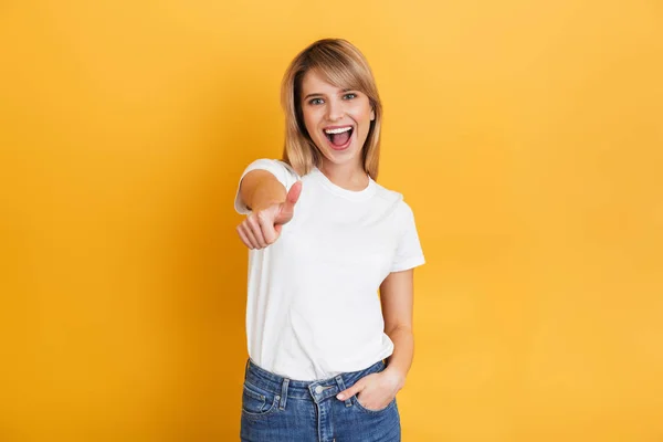 Lycklig ung Söt blond kvinna poserar isolerade över gul vägg bakgrund klädd i vit casual t-shirt. — Stockfoto