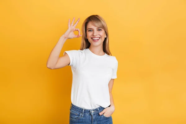 Весела щаслива приємна молода красива блондинка позує ізольована на жовтому фоні стіни, одягнена в білу повсякденну футболку, показуючи нормальний жест . — стокове фото