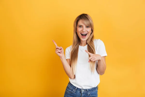 아름다운 행복 기쁘게 젊은 금발의 여자 포즈 고립 위에 고립 된 노란색 벽 배경 에 옷을 입고 흰색 캐주얼 티셔츠 가리키는 에 카피 스페이스. — 스톡 사진