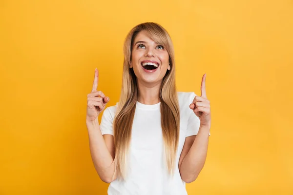 Surprised young excited shocked blonde woman posing isolated over yellow wall background pointing. — Stock Photo, Image