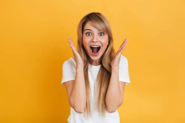 Shocked excited young blonde woman posing isolated over yellow wall background dressed in white casual t-shirt. — Stock Photo, Image