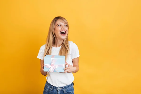 Lycklig ung upphetsad chockad blond kvinna poserar isolerade över gul vägg bakgrund Holding presentbox. — Stockfoto