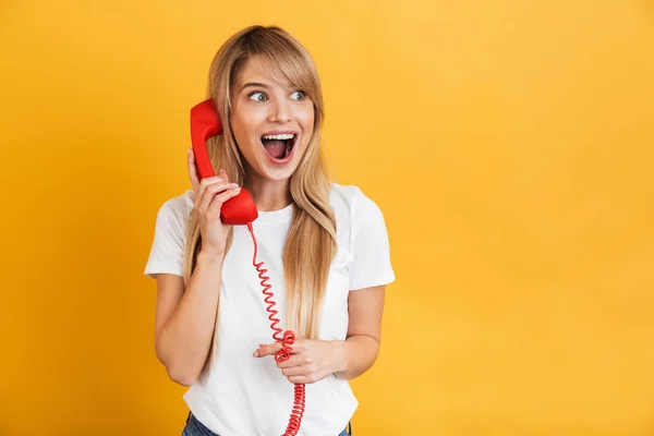 Feliz jovem animado chocado loira mulher posando isolado sobre amarelo parede fundo falando por retro vermelho telefone . — Fotografia de Stock