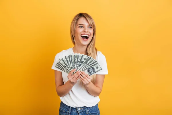 Screaming emotional young blonde woman posing isolated over yellow wall background dressed in white casual t-shirt holding money. — Stock Photo, Image