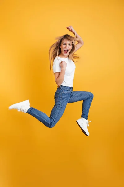 Emotionale Schreie positive junge blonde Frau springt isoliert über gelbe Wand Hintergrund gekleidet in weißen lässigen T-Shirt machen Siegergeste. — Stockfoto